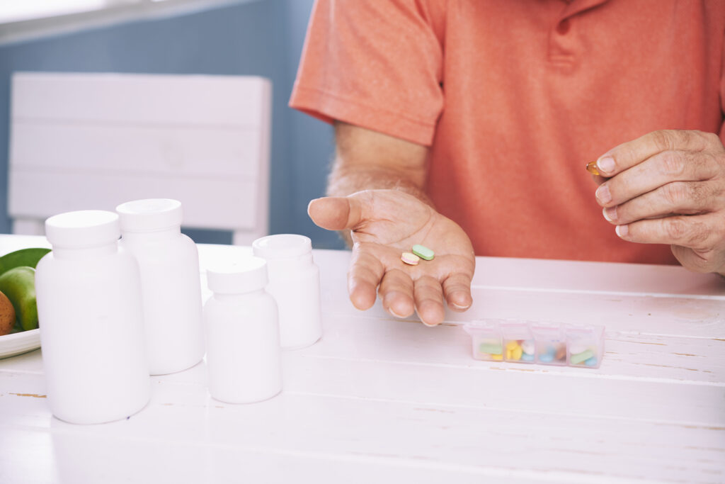 Senior taking daily medication with supplements on the table.