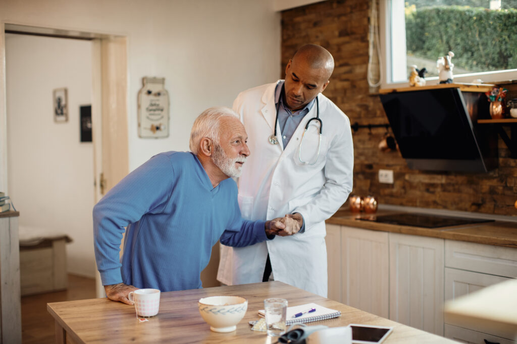 Doctor assisting senior man during a home visit, representing quality Medicare support and care.